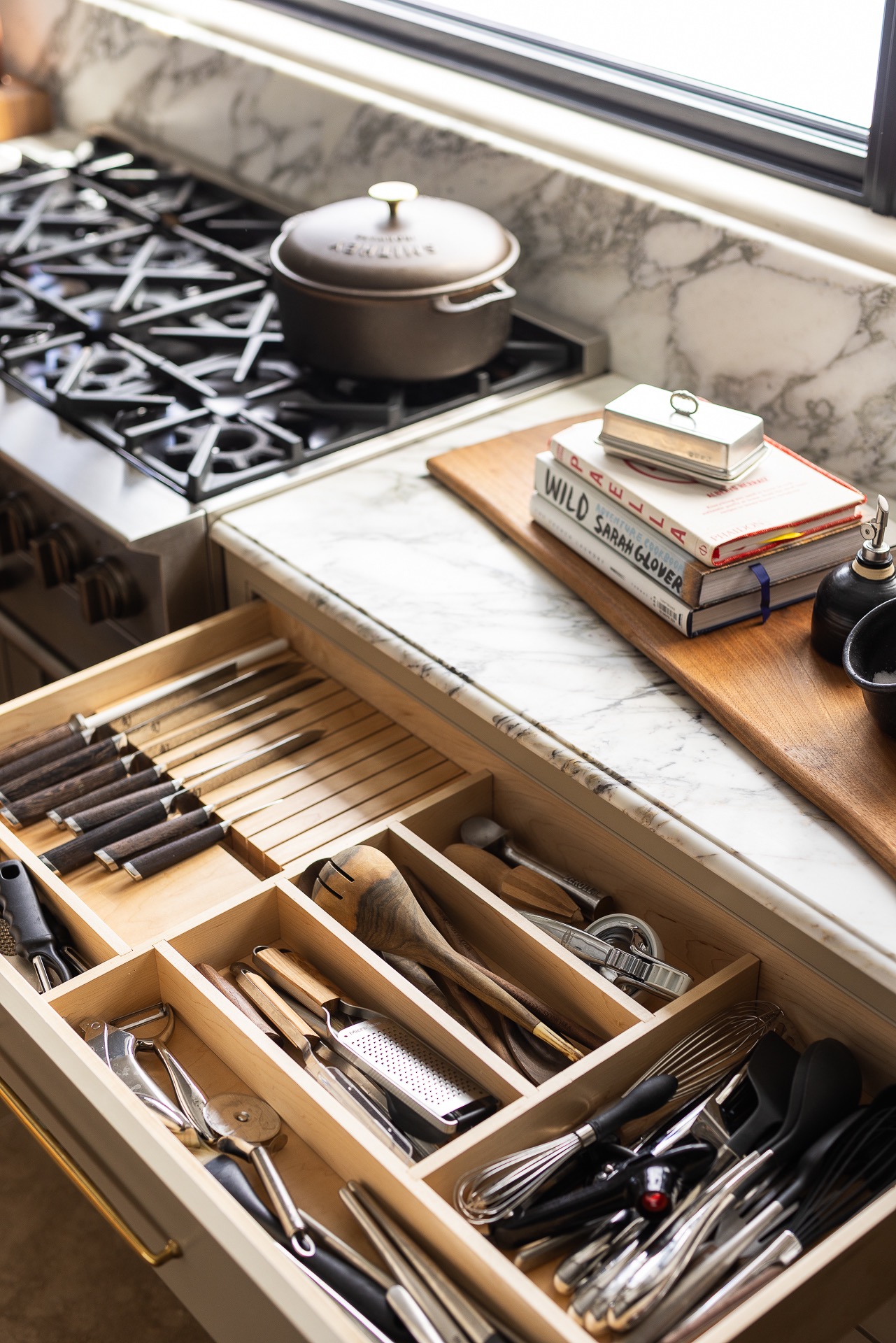 An open custom kitchen drawer filled with well-used cooking tools